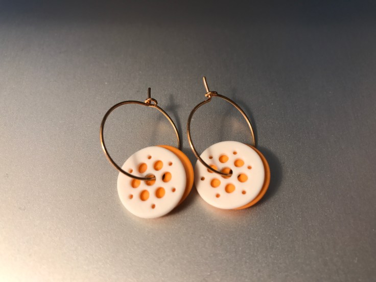 Gold Hoop Earrings from Priip in Copenhagen, Denmark that Have White Disks with Holes in Front of Coral Colored Disks