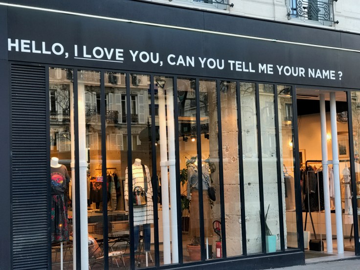 A photo of the exterior of the Leon & Harper boutique on Boulevard Beaumarchais in Paris, France. A sign in the front reads, "Hello, I love you, can you tell me your name?"