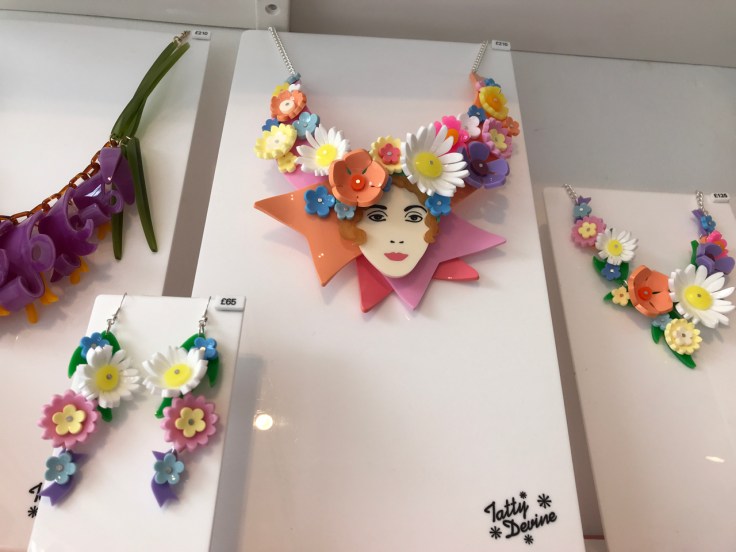 A photo of the, "May Flower," floral earrings and two of the, "May Flower Queen," necklaces from Tatty Devine. Tatty Devine is a local shop located in London, England. The pretty plastic jewelry features white, yellow, baby blue and pink flowers.