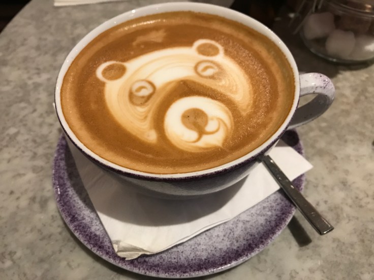 A photo of a cappuccino at Élan Café in London, England. The barista made a beautiful bear in the foam of this coffee drink.