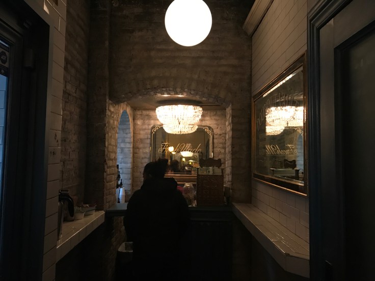 A photo inside the Doughnut Vault in Chicago, Illinois. The tiny donut shop space is decorated with subway tiles and is super small.