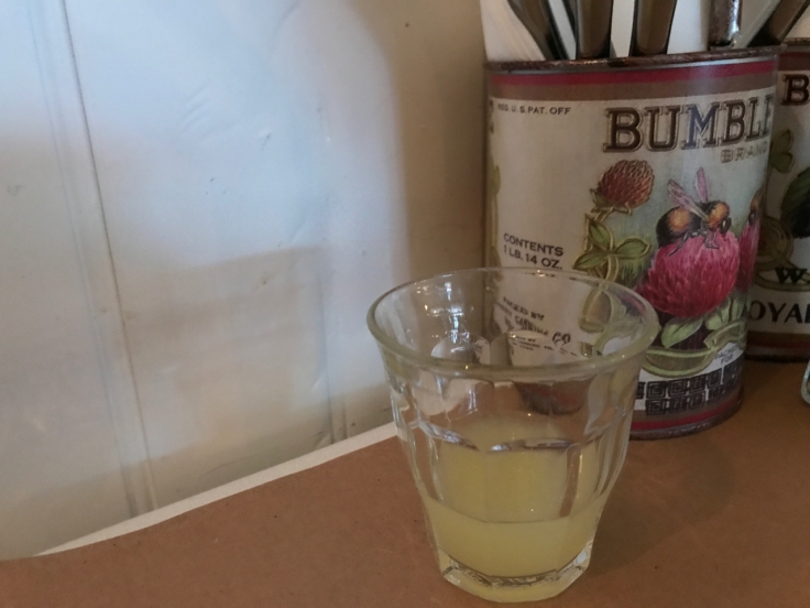 A photo of a shot glass filled with freshly squeezed chilled lemon juice on the table beside a Bumble Bee brand container filled with knives at Diane's Bloody Mary restaurant in San Francisco, California.