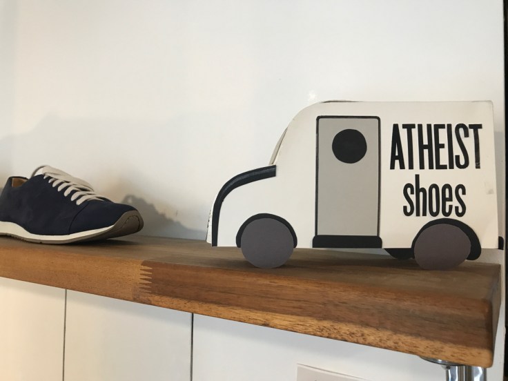 A photo of awfully black black sneakers and a little truck sign on a wood shelf at Atheist Shoes in Berlin, Germany.