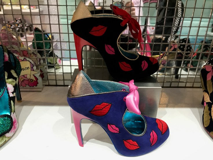 A photo of a black pair of high heels with red and pink embroidered lips on them beside a pair of navy blue high heels with red and pink lips embroidered on them at the Irregular Choice shoe store in London, England.