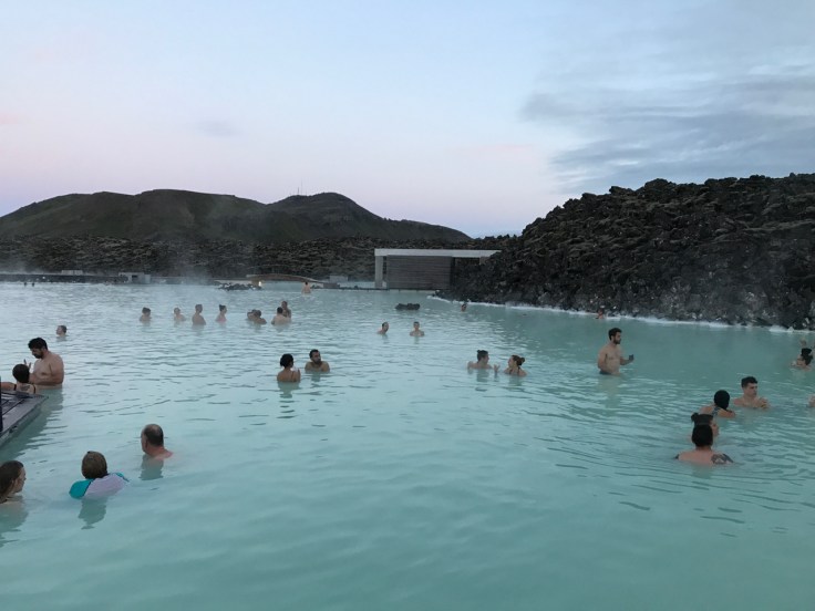 People swimming and bathing at sunset in the bright blue waters of Iceland's Blue Lagoon luxury geothermal spa just outside of Reykjavík in Grindavík, Iceland.