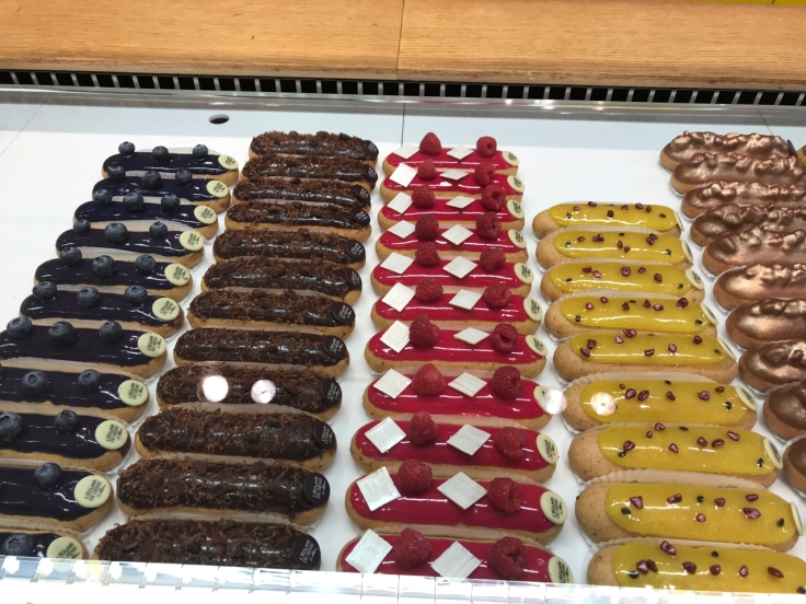 Beautifully hued blueberry (myrtille), chocolate, raspberry (framboise) and passion fruit (passion) éclairs sit in a display case at the Pavée location of L'Éclair de Génie pastry shop in Paris, France. Photo Courtesy of FoodWaterShoes