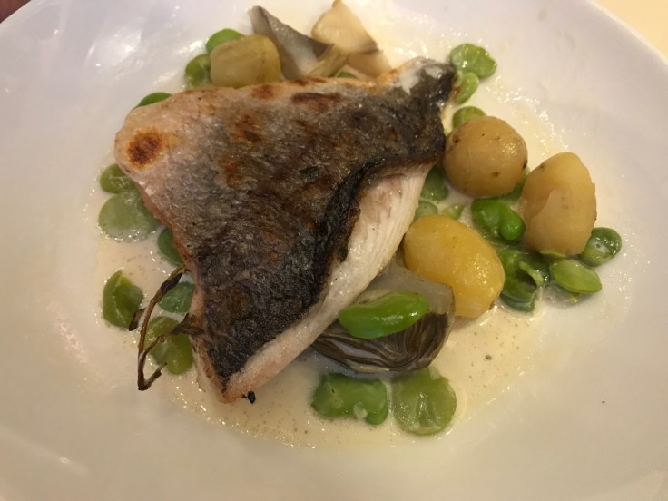 A plate of European sea bream surrounded by lemongrass emulsion, artichokes and potatoes (daurade royale, émulsion de coquillages à la citronelle, artichauts et pommes grenaille) at Au Pied de Cochon restaurant in Paris, France.