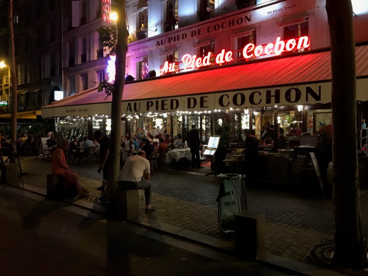 An exterior street view from the sidewalk outside of Au Pied de Cochon restaurant in Paris, France.