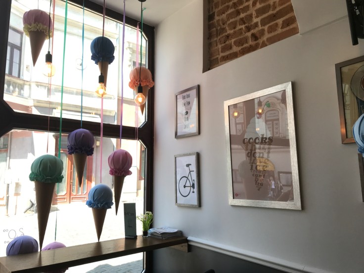 Brightly colored hand sewn ice cream cones hang in the window of the Ciekawa Słodko-Słono ice cream shop in Tarnów, Poland. A sign hanging on the wall says, "Cooks That Don't Love Ice Cream Can't Be Trusted."