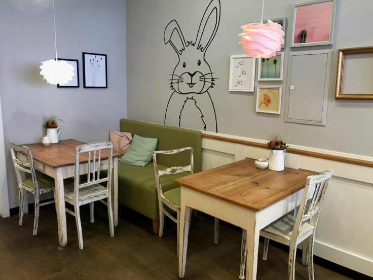 The interior tables and seating at Katjes Café Grün-Ohr coffee shop in Berlin, Germany feature their bunny rabbit mascot stenciled on the wall behind them. Photo Courtesy of FoodWaterShoes