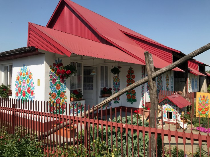 A white house with a red roof that has brightly colored flowers painted on the sides of its walls in Zalipie, Poland.