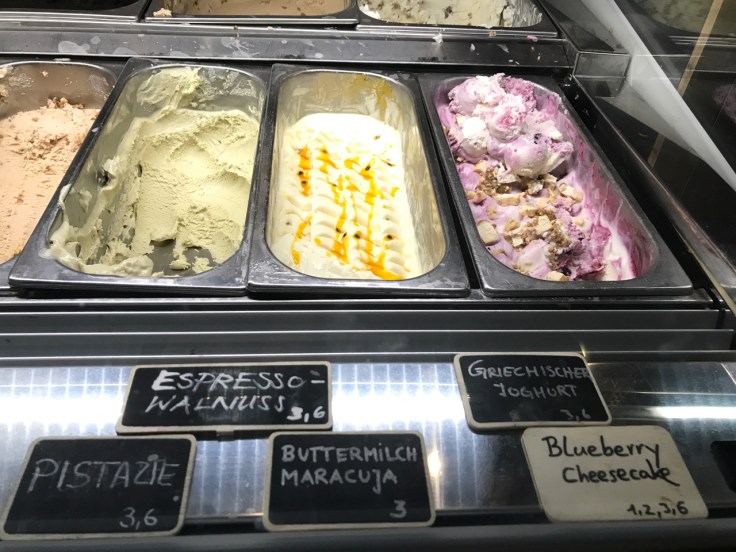 Containers filled with pistachio (pistazie), espresso walnut (espresso walnuss), buttermilk passionfruit (buttermilch maracuja), greek yogurt (Griechischer yoghurt) and blueberry cheesecake at Claus Eismanufaktur & Deli ice cream, gelato, sorbet shop, café and restaurant in Stuttgart, Germany.