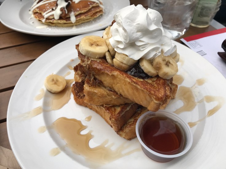 A plate is piled high with PBB&J Texas style French toast topped with sliced bananas, whipped cream and powdered sugar at Mo's Breakfast + Burger Joint in Campbell, California. Photo Courtesy of FoodWaterShoes