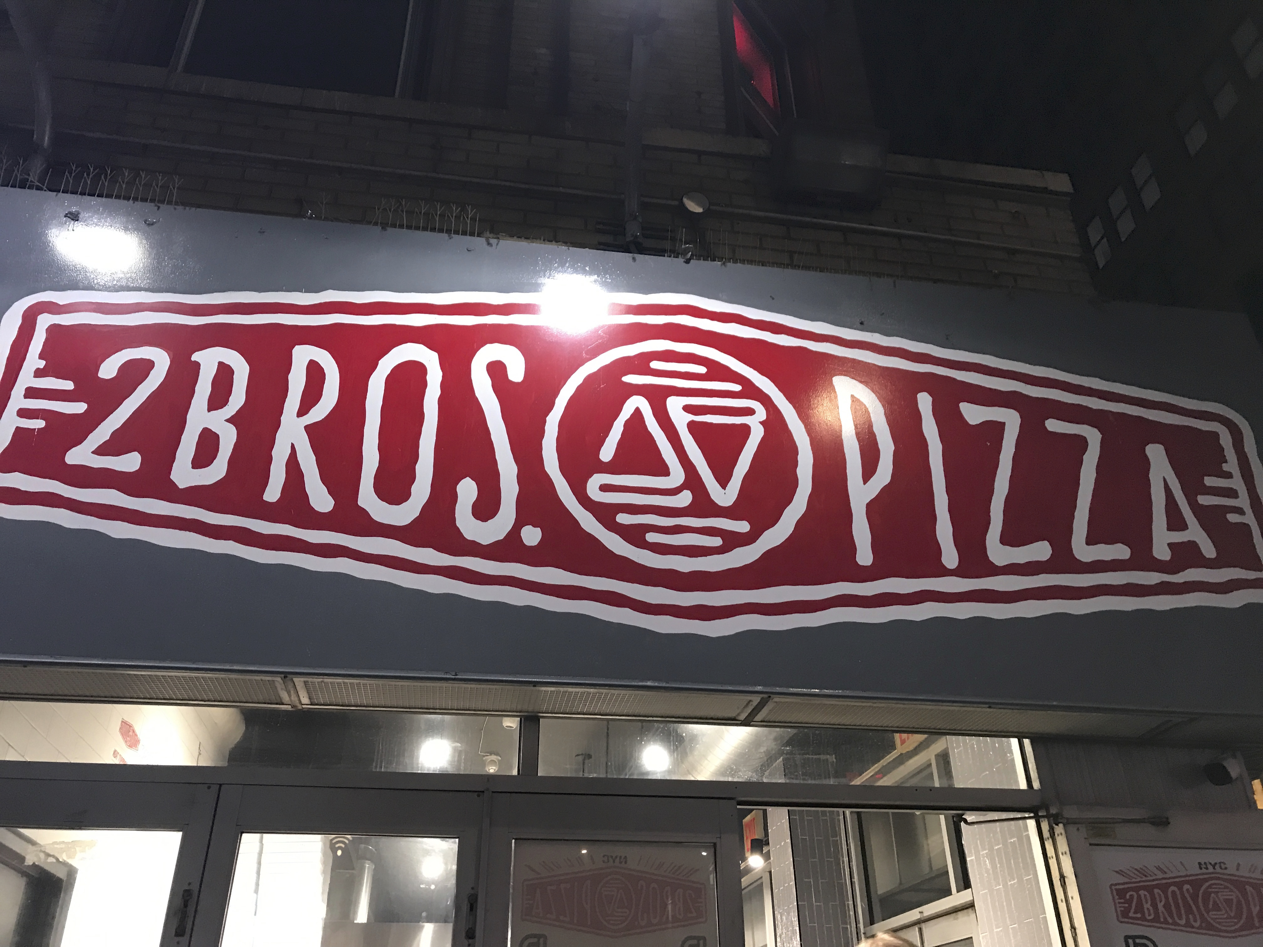 An exterior street view photo of the outside front of 2 Bros. Pizza in New York City, New York. Photo Courtesy of FoodWaterShoes.