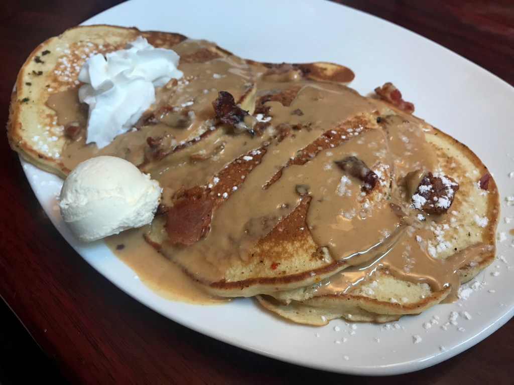 A photo of the Elvis B-side at Modern Malt in Syracuse, New York. The dish consists of three bacon and banana stuffed pancakes topped with peanut butter drizzle. Photo Courtesy of FoodWaterShoes