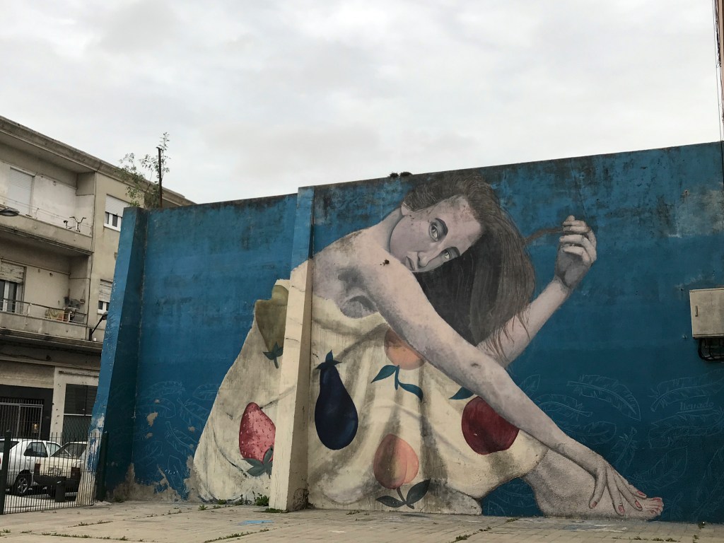 A photo of graffiti by Colectivo Licuado (which consists of street artists Camilo Núñez and Florencia Durán) in Montevideo, Uruguay. The wall mural features a woman (or a girl) in a dress covered with fruit and is one of the sights to see / things to do in Montevideo.