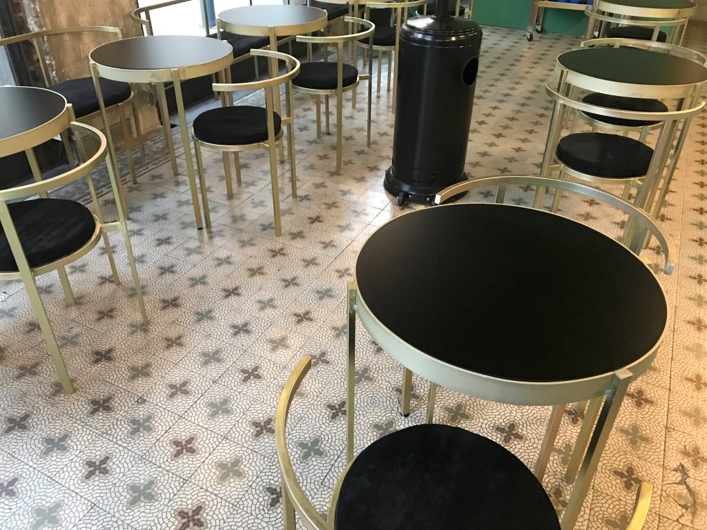 A photo of a pretty tiled floor topped with elegant gold chairs and tables at Nómade, a café in Montevideo, Uruguay. Photo Courtesy of FoodWaterShoes