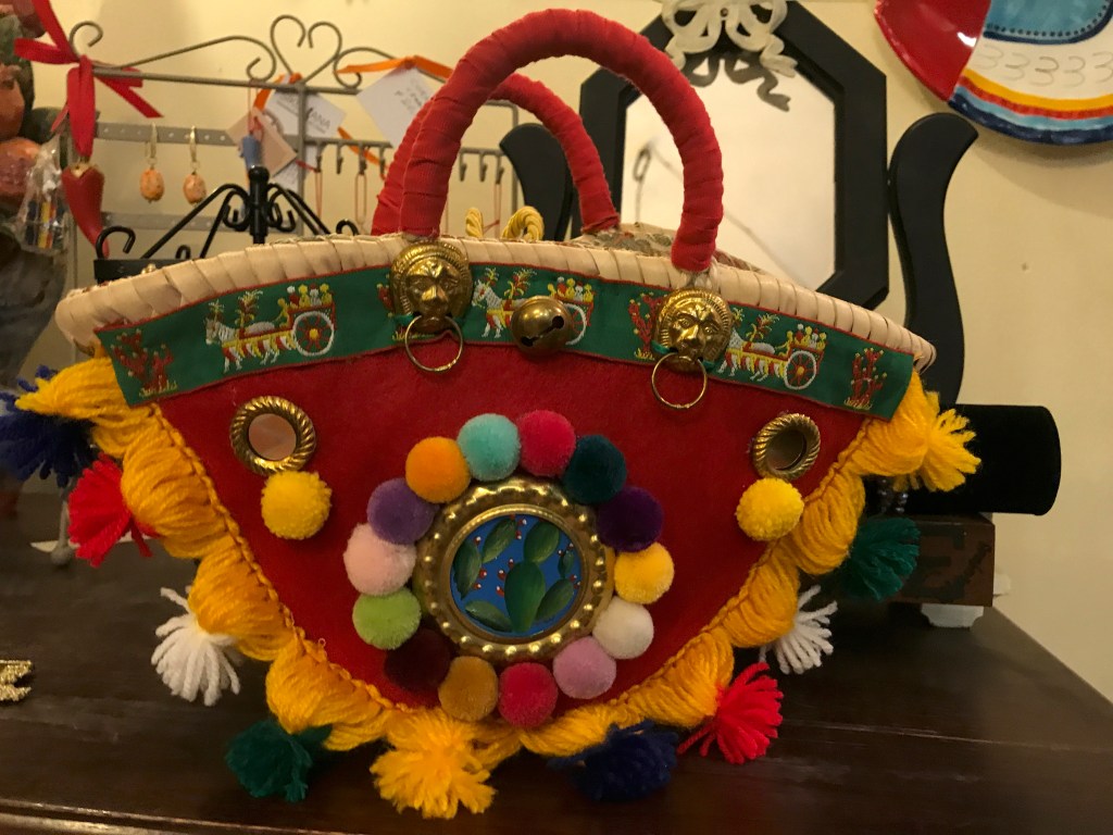 A photo of a handmade red basket bucket bag with colorful pompoms at Sikuliana Art Atelier in Florence, Italy. Photo Courtesy of FoodWaterShoes