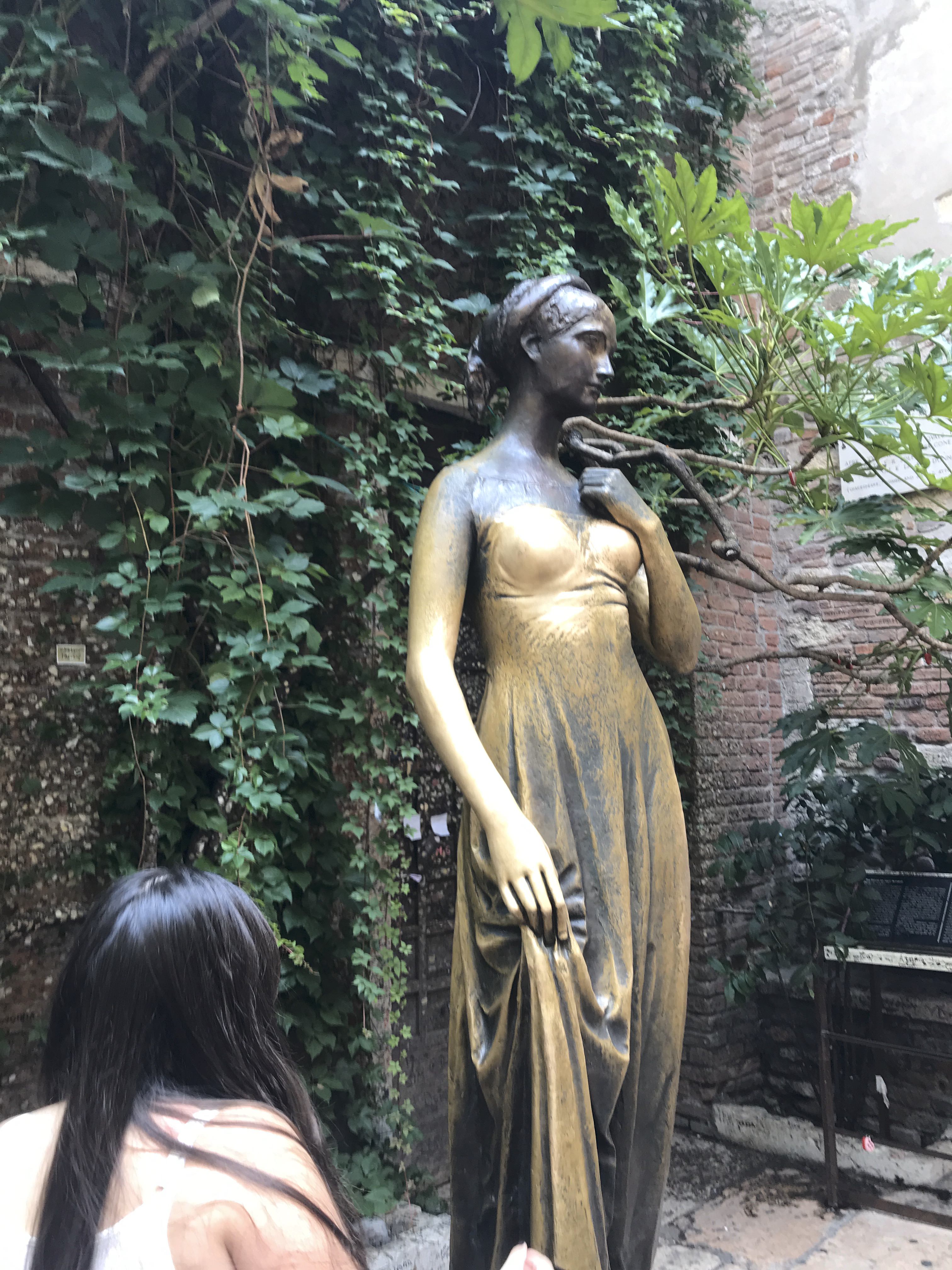 A photo of a tourist looking at the gold statue of Juliet in a courtyard in Verona, Italy. Photo Courtesy of FoodWaterShoes