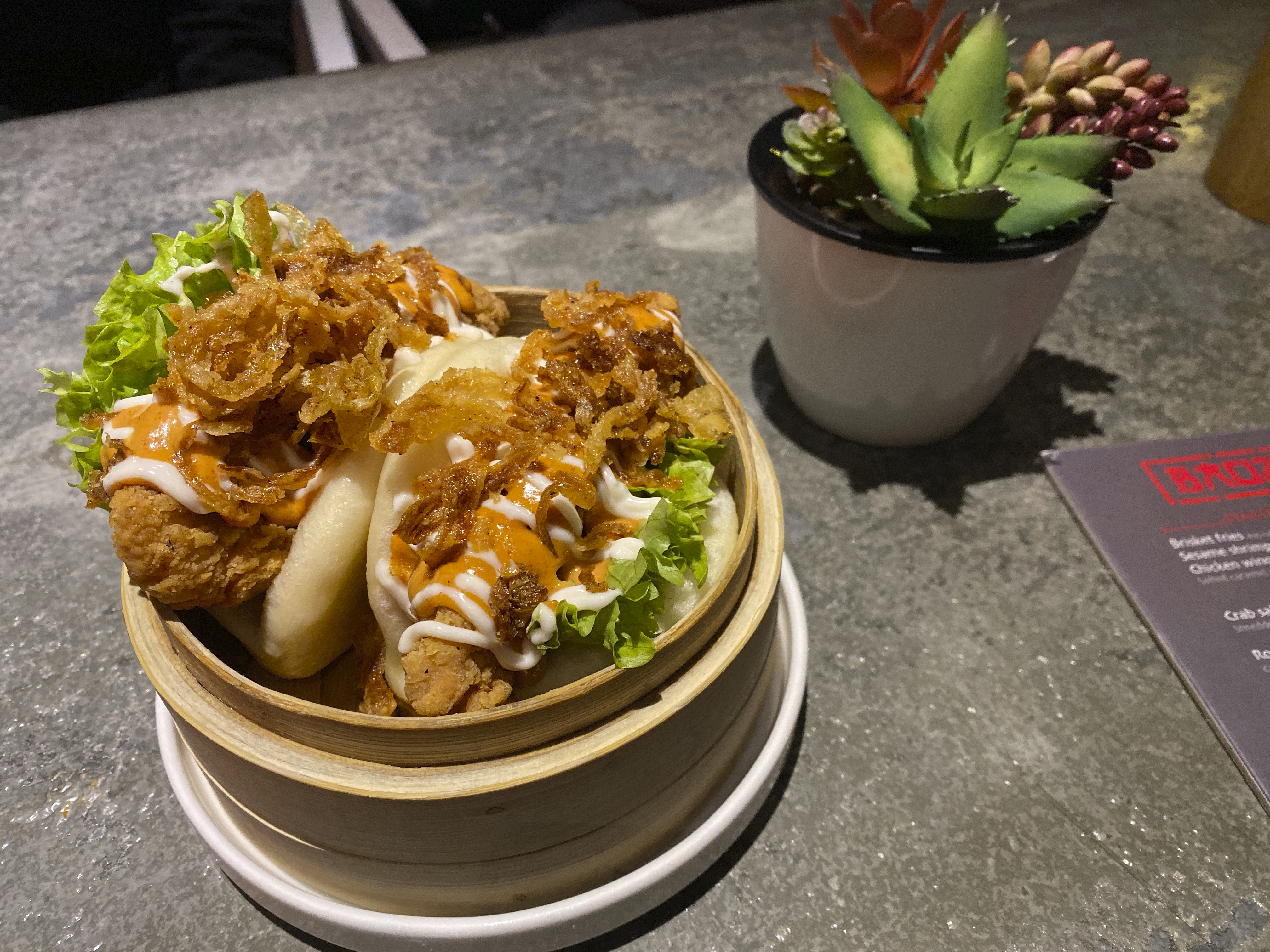 A photo of fried chicken loca baos with crispy onions and chipotle sauce on a table at Baozi باوزي restaurant in Riyadh, Saudi Arabia. Photo Courtesy of FoodWaterShoes